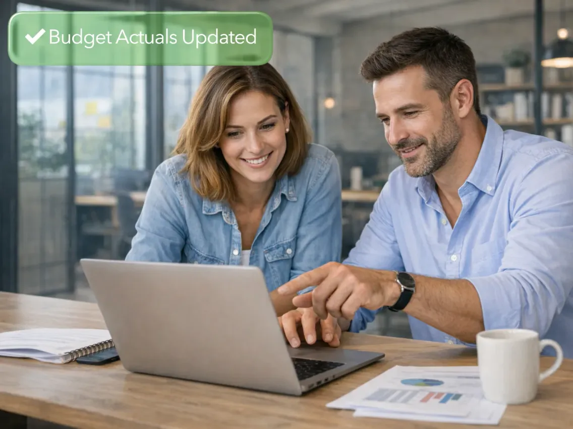 Two colleagues reviewing figures on a laptop, with a "Budget Actuals Updated" confirmation